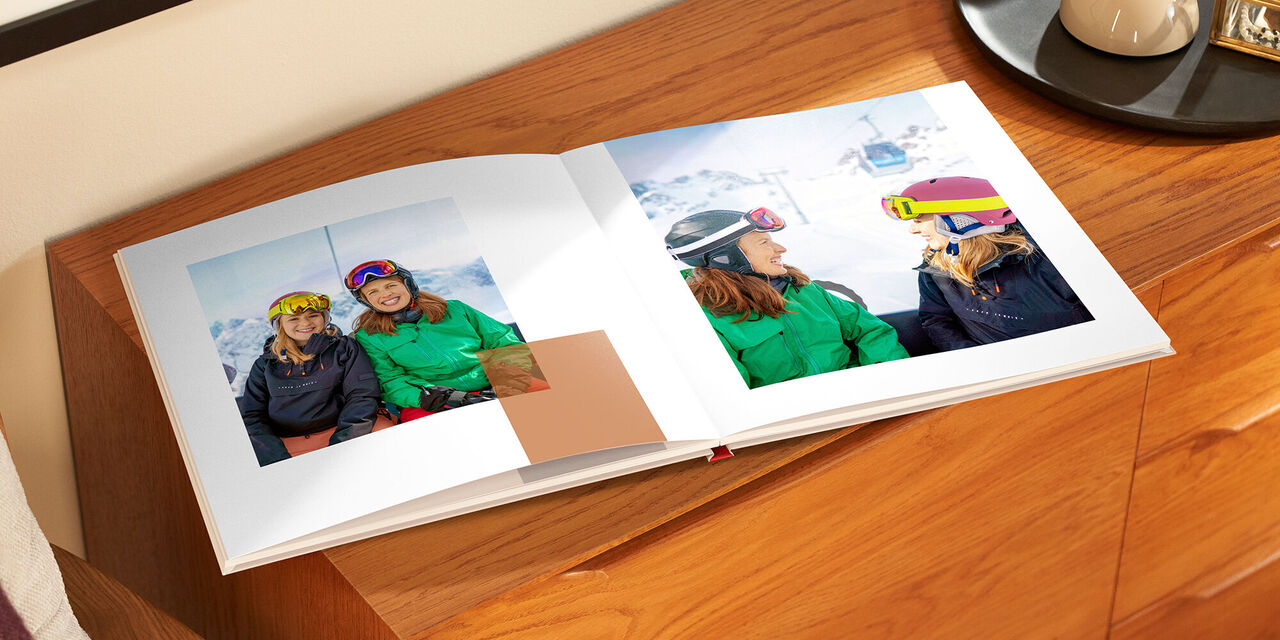 Sur une étagère en bois se trouve le livre de photos ouvert. Les deux pages présentent des photos de deux femmes sur une piste de ski.