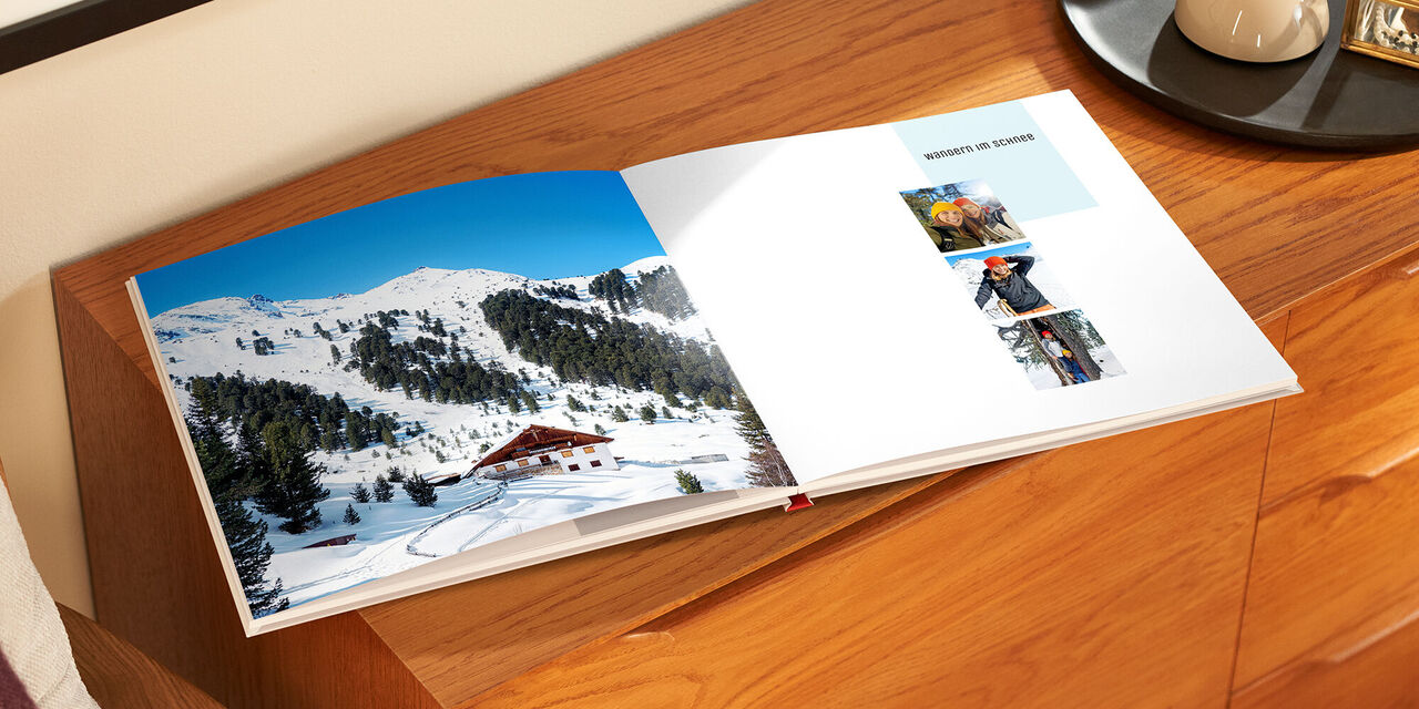 Le livre de photos ouvert est posé sur un meuble en bois. À gauche, on voit une photo pleine page représentant une auberge devant une chaîne de montagnes enneigées. Sur la page de droite, trois photos carrées sont disposées, présentant chacune deux femmes.